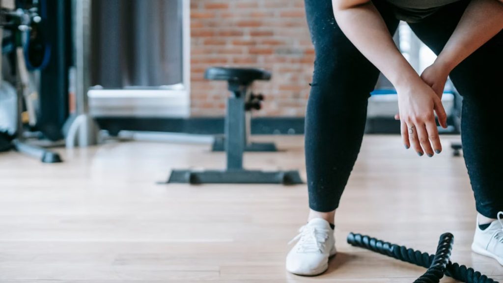 Crop anonymous female in sportswear resting after workout with ropes in gym with sports equipment